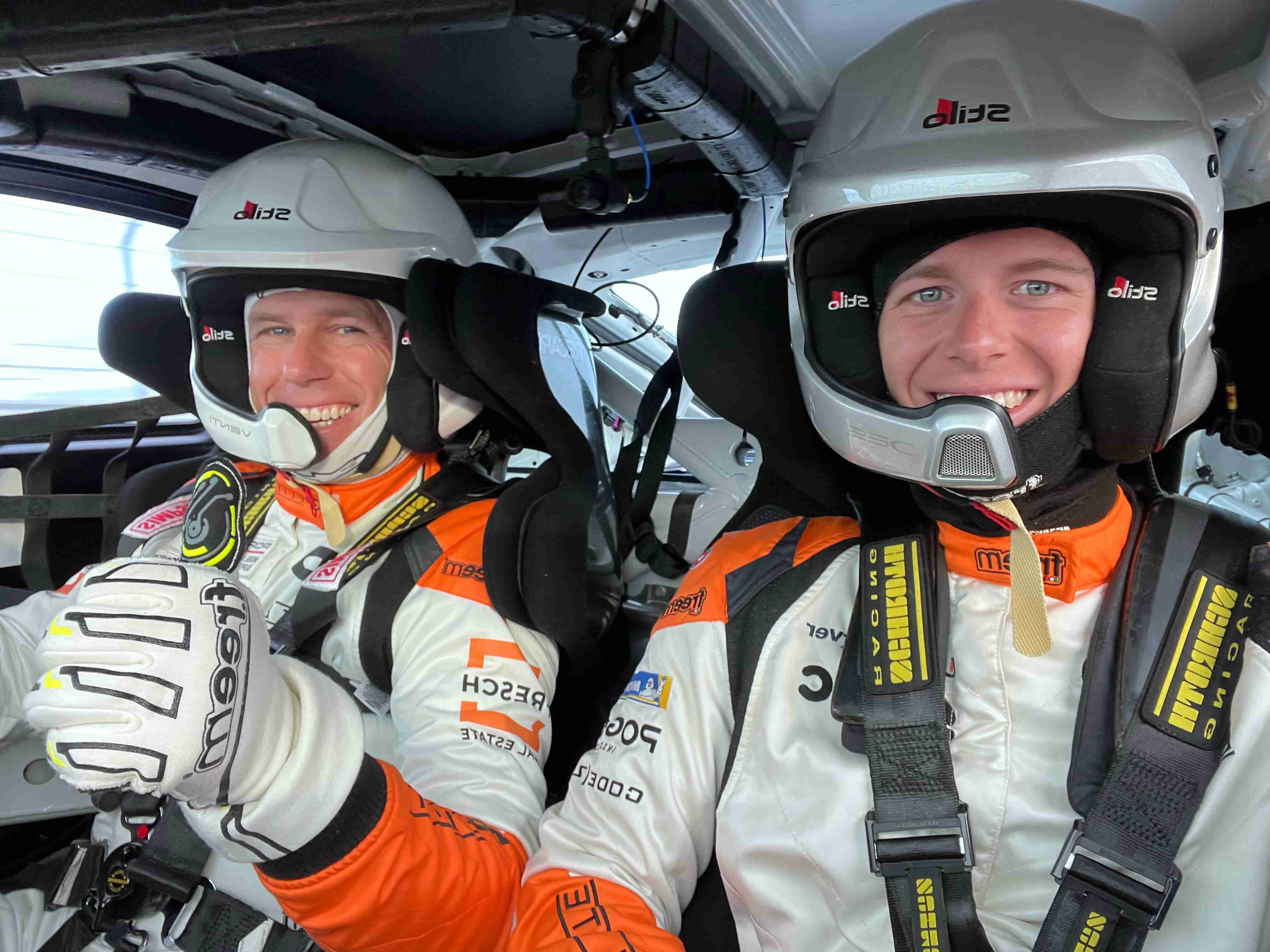Two racing drivers in cockpit wearing helmets